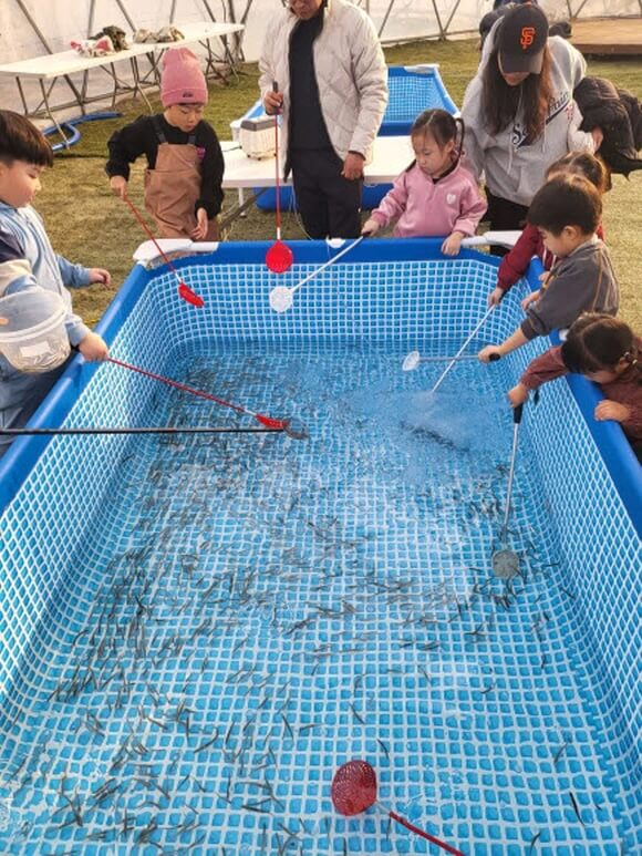 아이들이 대형욕조에서 작은뜰채로 빙어를 뜨는 모습
