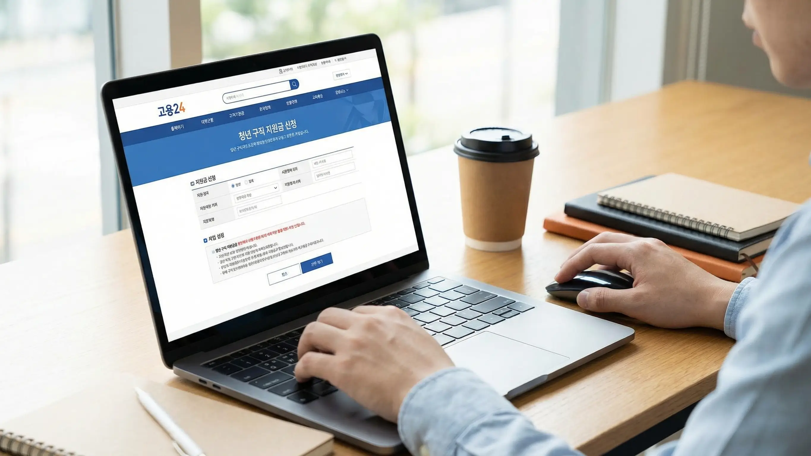 노트북 화면에 고용24 홈페이지를 띄워놓고 구직 지원금을 신청하는 청년의 손 클로즈업