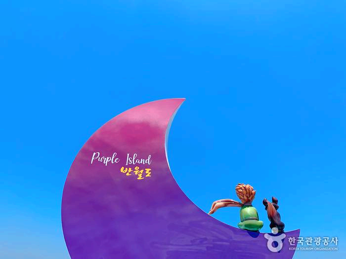 반달모양 표지판 위에 어린왕자 모형이 앉아있다.