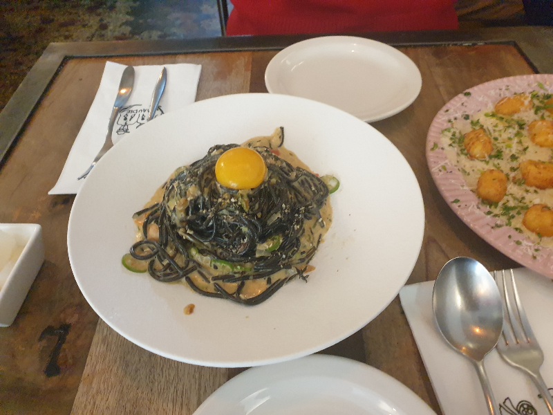 초록면과 계란 노른자로 특색 있는 우니 톳 크림 파스타가 우드 테이블 위에 올려져 있다.