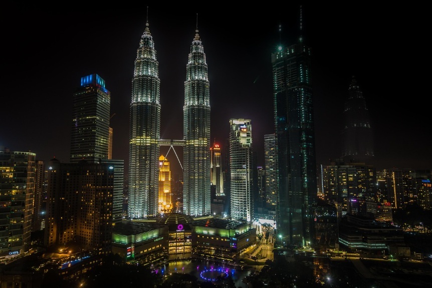 짙은 밤하늘 아래 화려하게 빛나는 말레이시아 쿠알라룸푸르의 페트로나스 트윈 타워와 주변 현대적인 마천루들이 어우러진 도심 야경 전경
