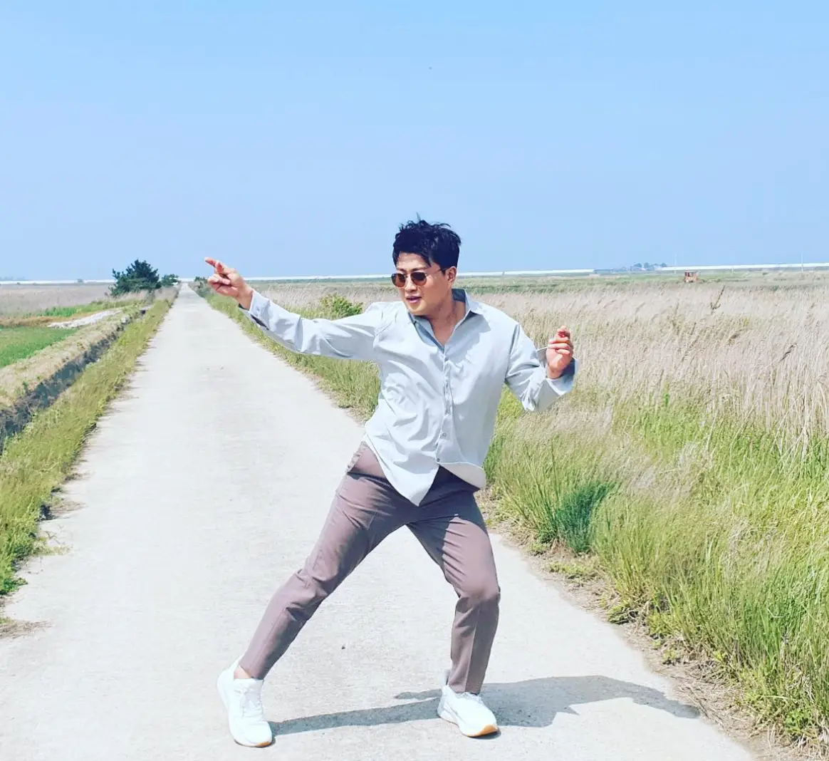 초록 들판 사이 난 회색 길위에서 흰셔츠 갈색 바지를 입고 춤추고 있는 김호중