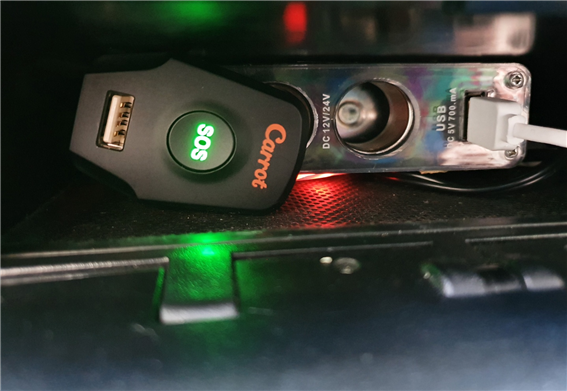 차량 시거잭에 꽂혀 녹색 불빛이 켜진 캐롯 플러그, SOS 버튼과 USB 포트가 보이는 모습
