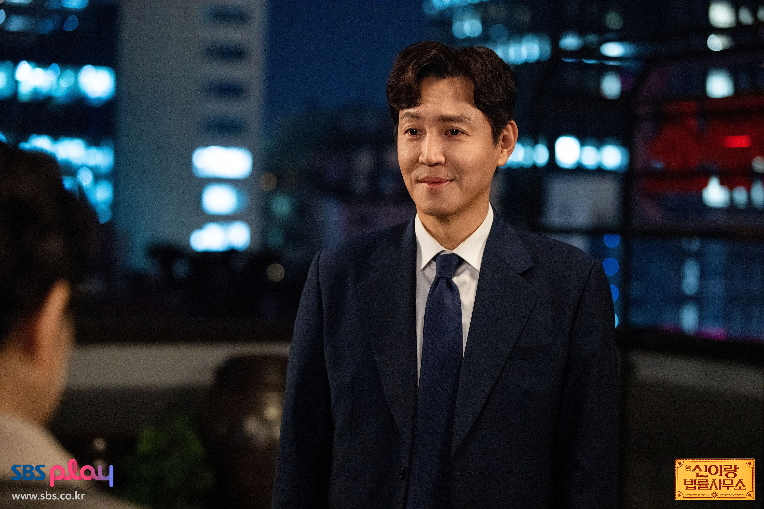 신이랑 법률사무소 최종회 공식 스틸에서 남색 정장을 입은 남성이 상대를 바라보는 장면