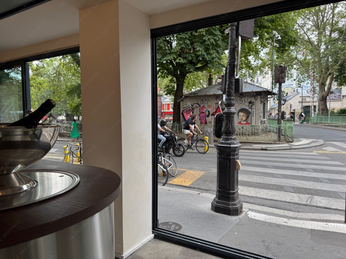 View from inside MIKE pizza shop looking out a large open window onto a Paris street crossing near the canal