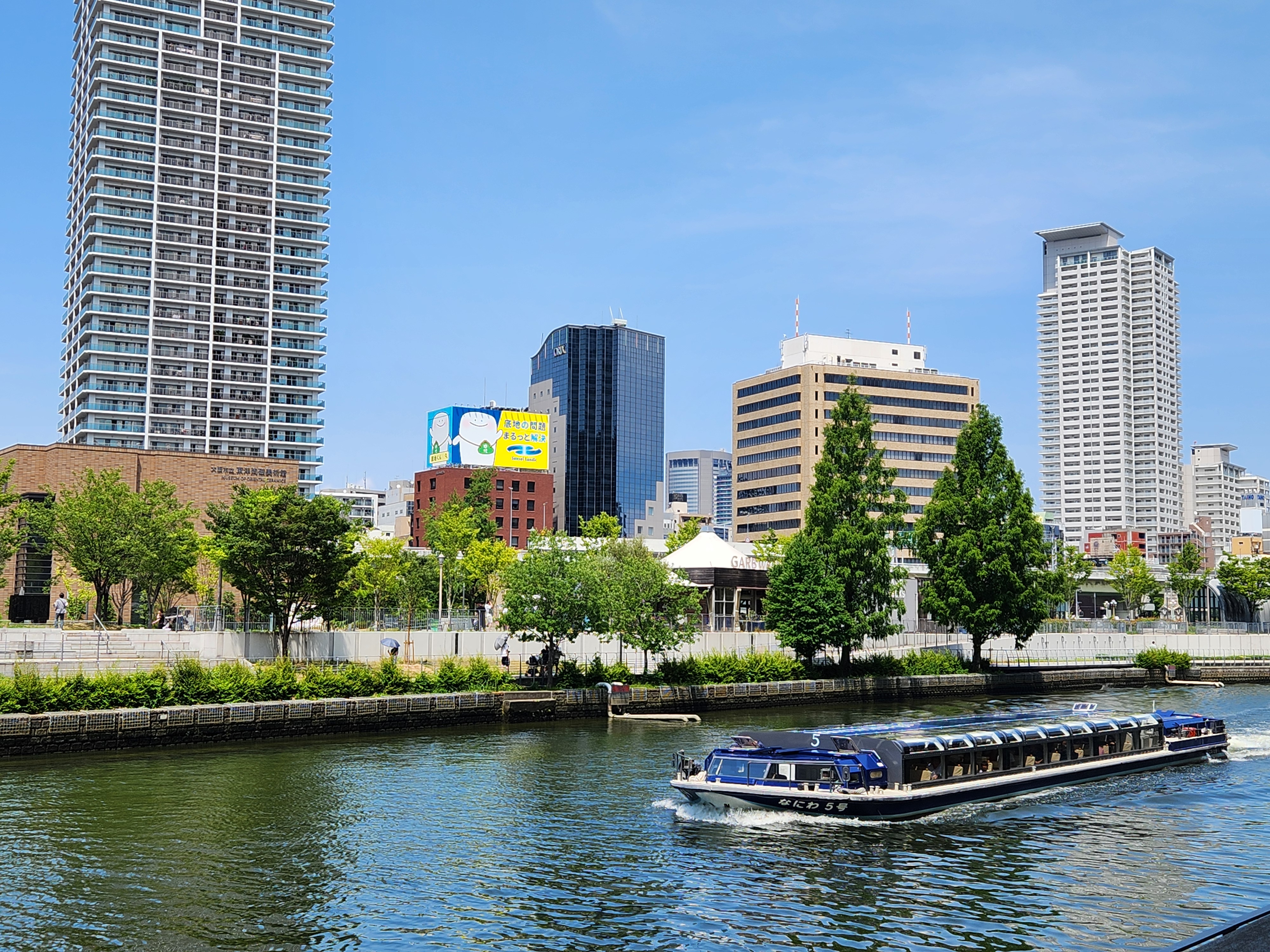 강 위를 천천히 지나가는 유람선과 오사카 중앙공회당이 보이는 강변 풍경