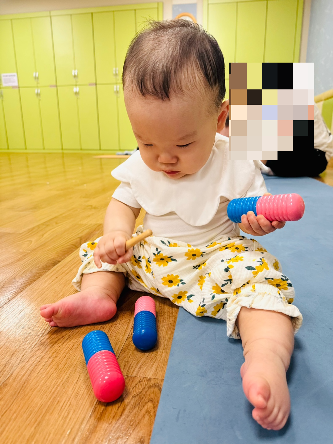 분홍색과 파란색 실로폰 장난감을 바라보며 앉아있는 9개월 아기