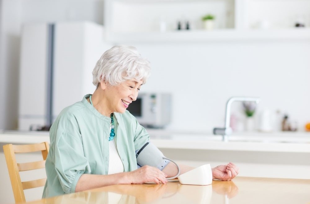 한 시니어 여성이 웃으면서 스스로 혈압을 측정하는 모습 via canva