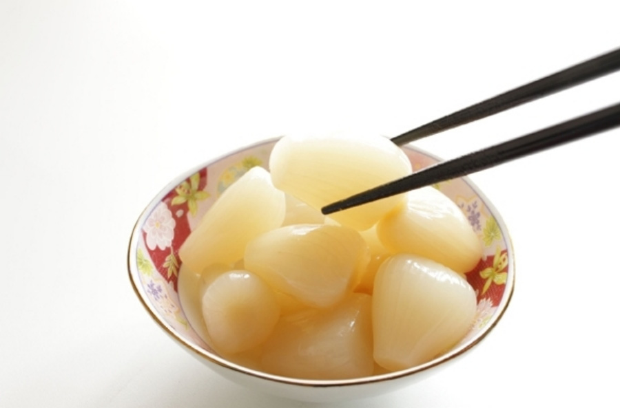 염교 알맹이를 깨끗하게 세척한 후에 식초에 절여서 만든 염교장아찌를 꽃무늬가 그려진 동그란 작은 그릇에 놓아두고 젓가락으로 하나를 집고 있는 것을 찍은 사진