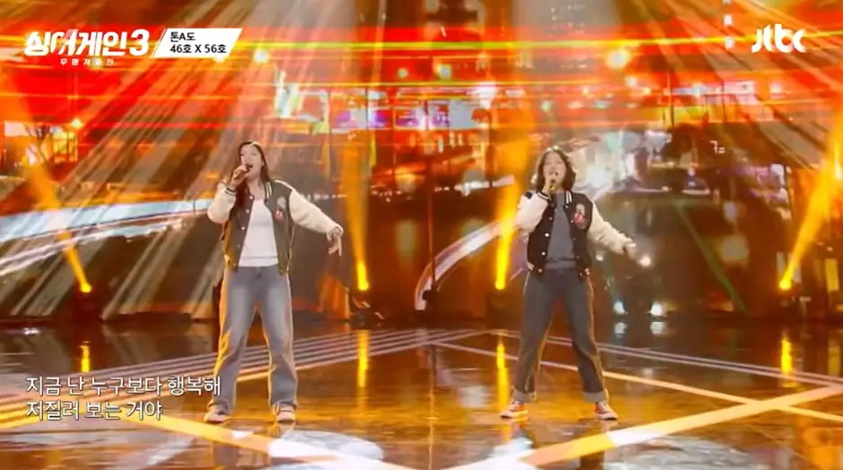 싱어게인 3- 무대 오른쪽 검정색 몸통에 흰색팔부분 점퍼를 입고 단발 곱슬머리상태로 오른손으로 마이크를 쥐고 청바지를 입은채 노래하는 56호와 무대 왼쪽 청바지에 검정색 쟈켓을 입고 오른손에 마이크를 든채 노래하는 46호