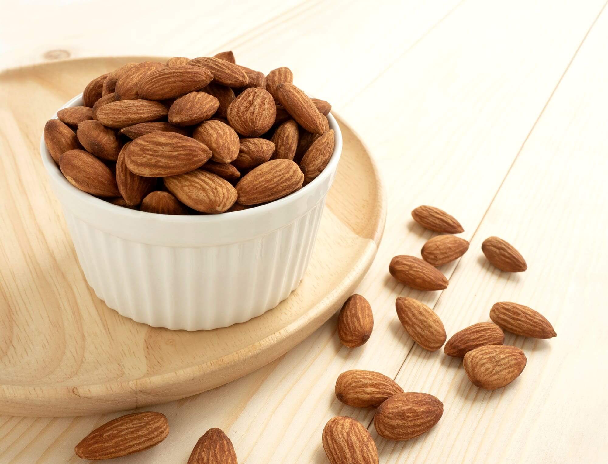 화이트 그릇에 담긴 아몬드, 원목 배경 위에 흩어진 견과류