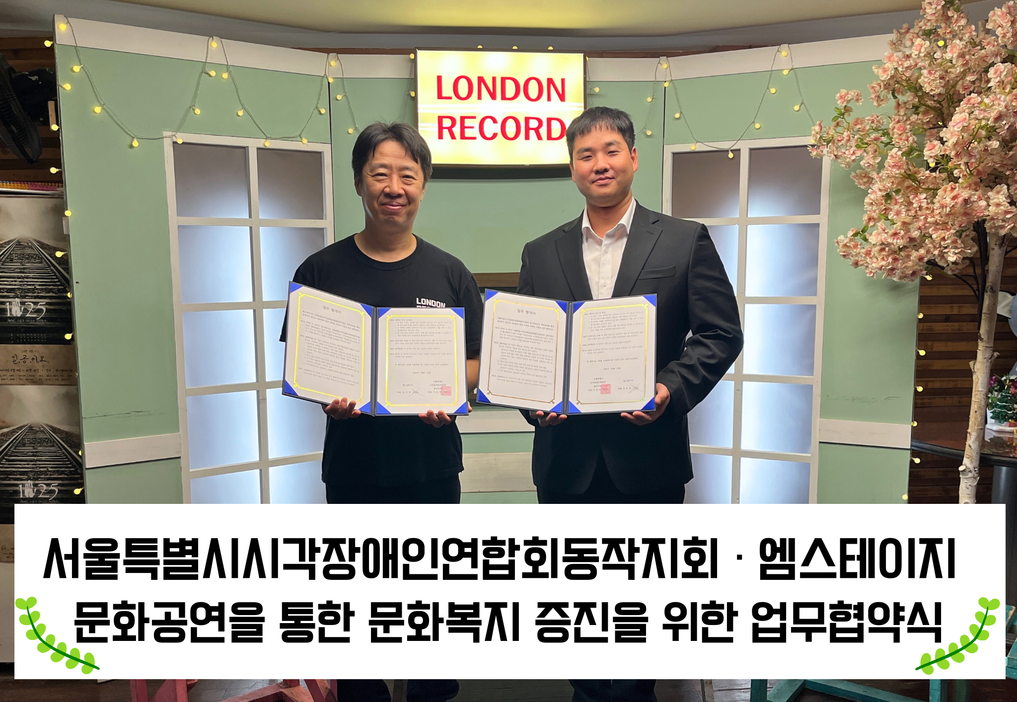 좌측부터 엠스테이지 김인성대표와 서울특별시시각장애인연합회 동작지회 이승민 동작지회장이 협약서를 들고 함께 사진을 찍고 있다. 하단에는 서울특별시시각장애인연합회동작지회, 엠스테이지 문화공연을 통한 문화복지 증진을 위한 업무협약식이라고 쓰여져있다.