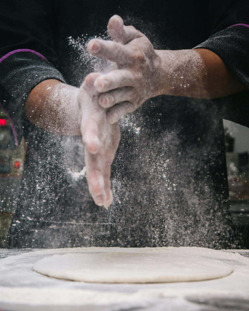 도우 반죽을 넓게 펴고 밀가루를 치고 있다.