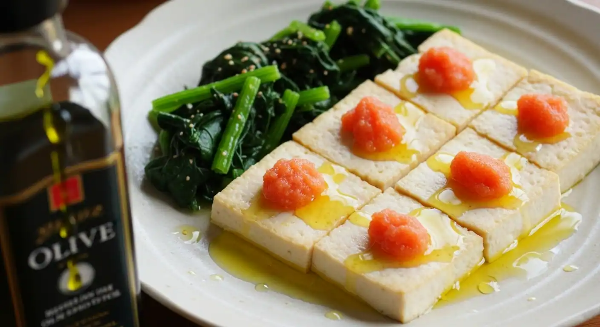 두부 위에 명란과 올리브유가 뿌려져 있으며, 데친 시금치가 접시에 놓여 있음