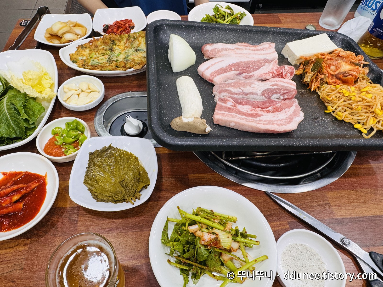 장수오리삼겹 생삼겹살이 올라간 불판과 김치, 콩나물, 다양한 밑반찬이 가득 차려진 기본 상차림