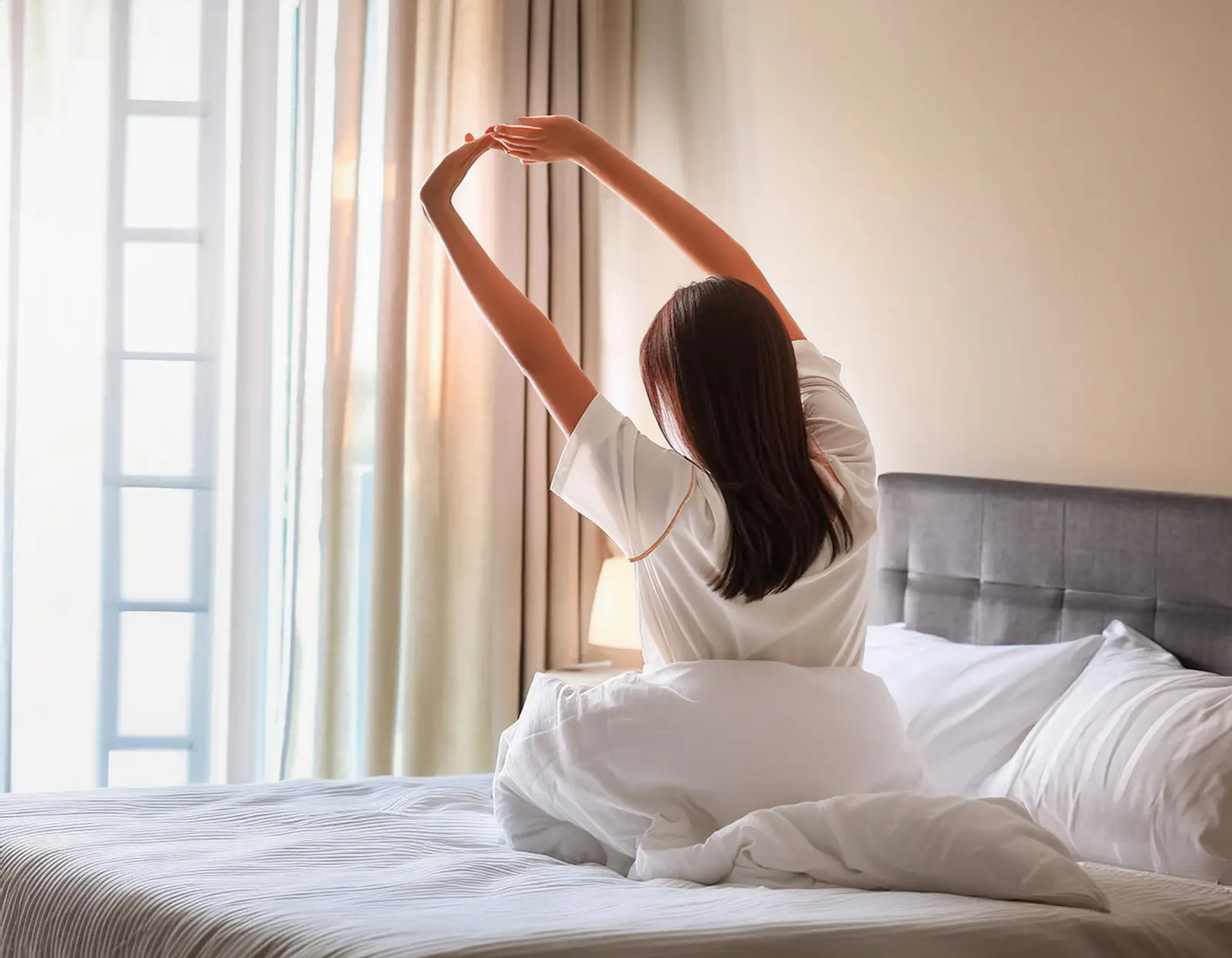침대에서 일어나 기지개를 켜는 여성