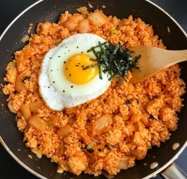 후라이팬에 김치볶음밥이 담겨 있고, 위에 반숙 계란과 김가루가 올려진 모습