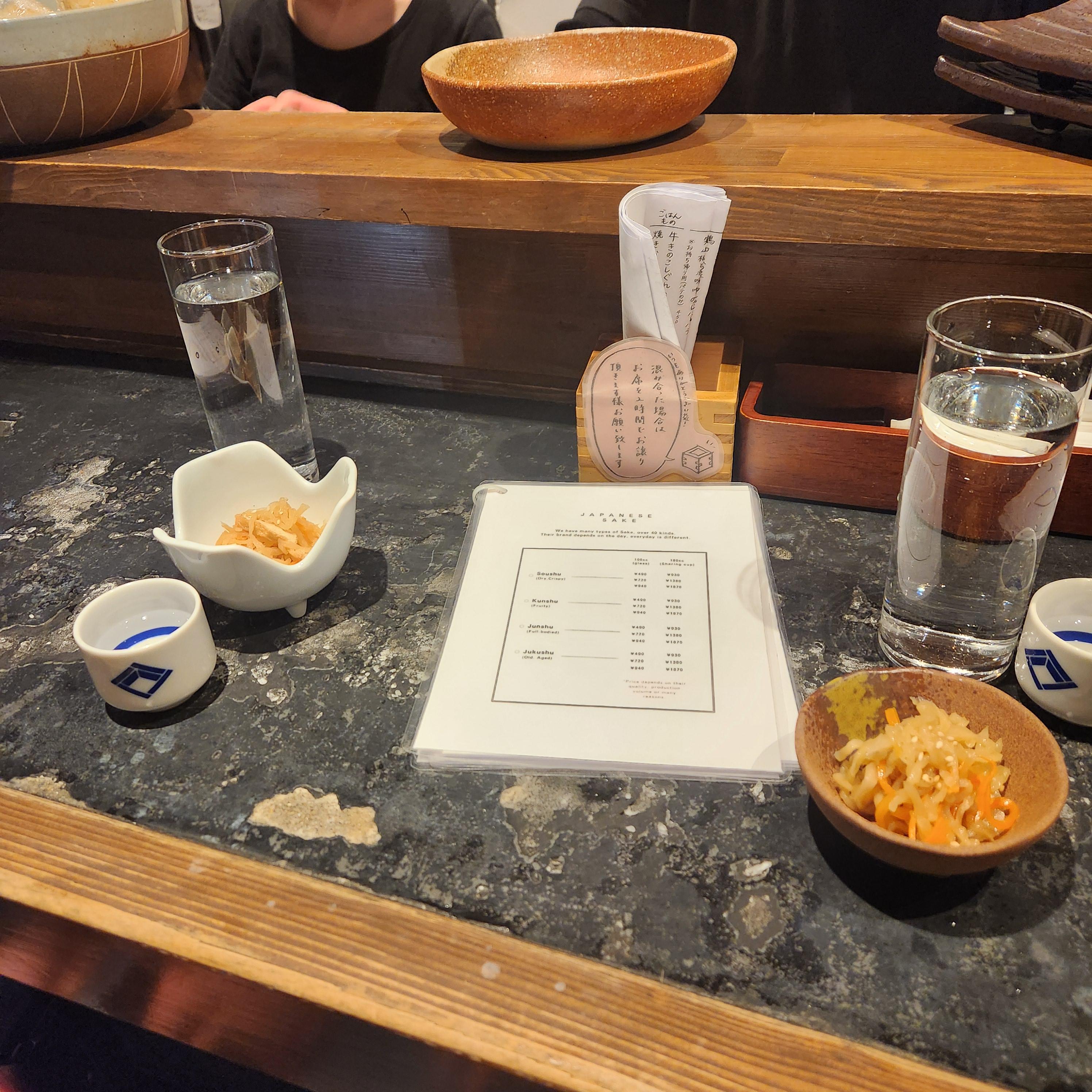 테이블 위에 기본 반찬과 물 그리고 메뉴판이 놓여있다.