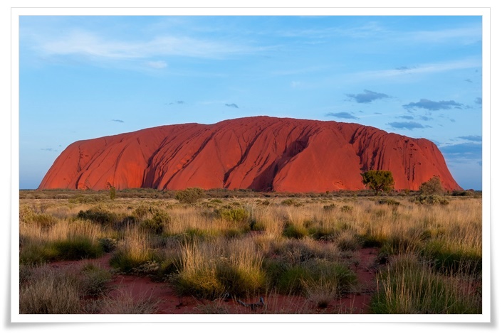 사막 한 가운데 솟아오른듯이 거대한 붉은 바위가 신비로운 모습으로 자리잡고 있는 풍경
