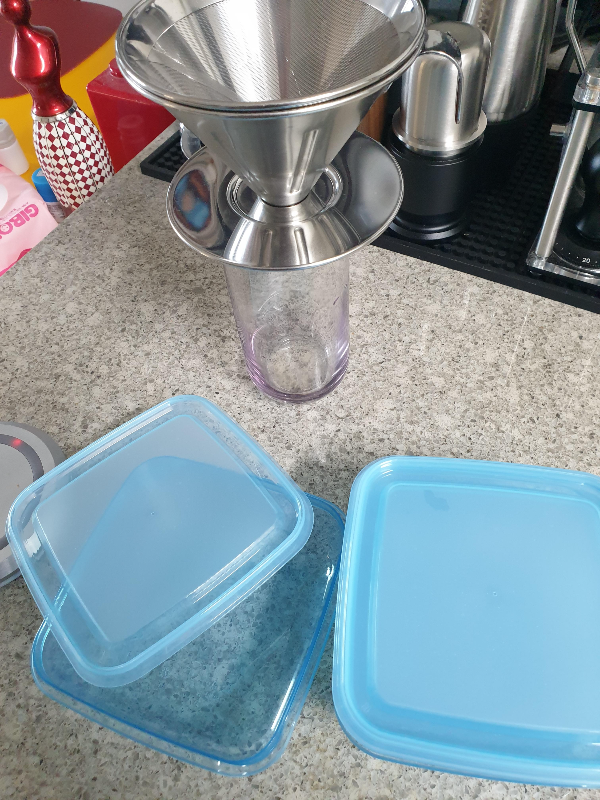 테이블 위에 메탈 드리퍼와 파란색 식품 저장 용기 3개가 놓여 있다.