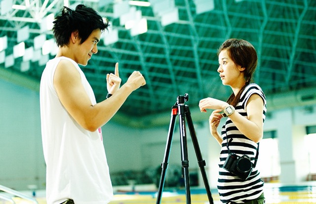 영화 《청설》에서 수영장 한쪽, 삼각대 앞에 선 두 주인공이 수화로 대화를 나누는 장면. 말 없이도 통하는 마음, 청춘의 맑고 조심스러운 떨림이 화면을 가득 채운다.