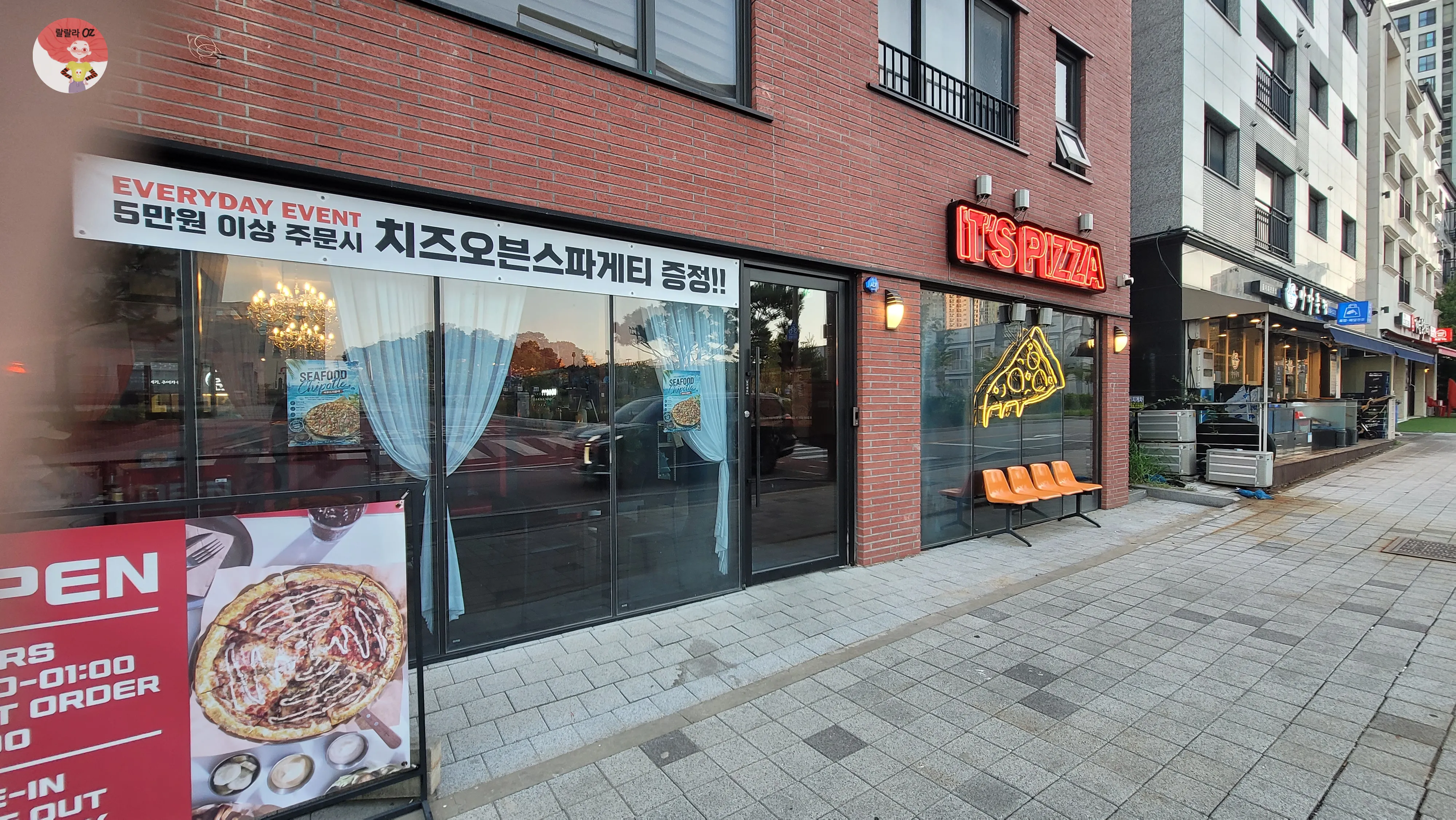 ‘IT’S PIZZA’ 네온사인과 피자 조각 모양 불빛, 주황색 의자가 놓인 이츠피자 다산점 입구