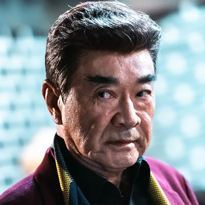 어느 실내를 배경으로 백발을 올린고 빨간 슈트를 입고 서 있는 드라마 7인의 탈출의 방칠성 캐릭터