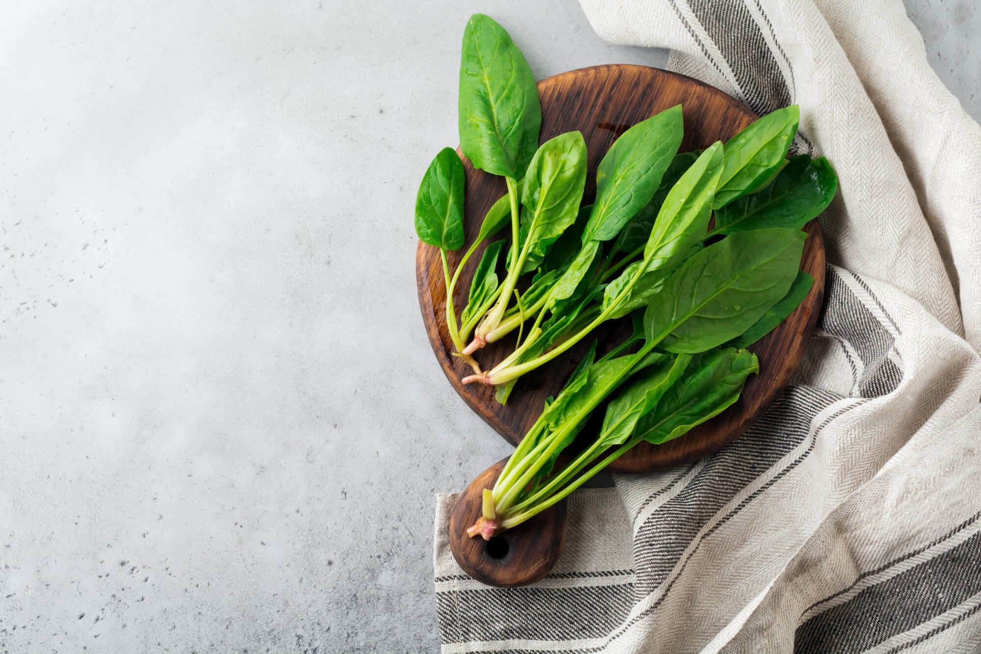 나무 도마 위에 올려진 시금치, 밝은 그레이톤 주방 타월과 함께