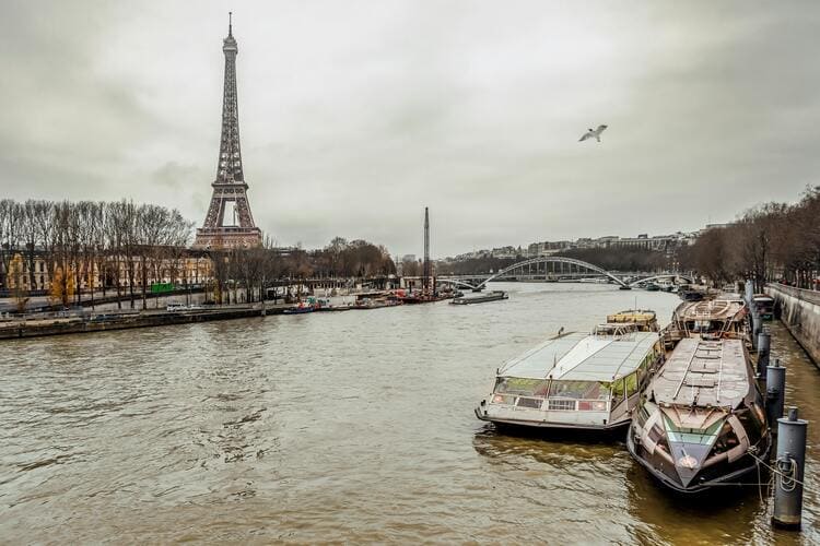 흐린 날씨 속 세느강과 정박된 유람선들 사이로 에펠탑이 보이는 파리의 겨울 정취가 묻어나는 장면