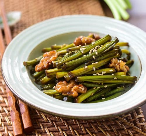 접시에 담긴 윤기 나는 마늘쫑볶음과 호두, 고소한 참깨가 어우러져 건강하고 담백한 저염 한국 밑반찬