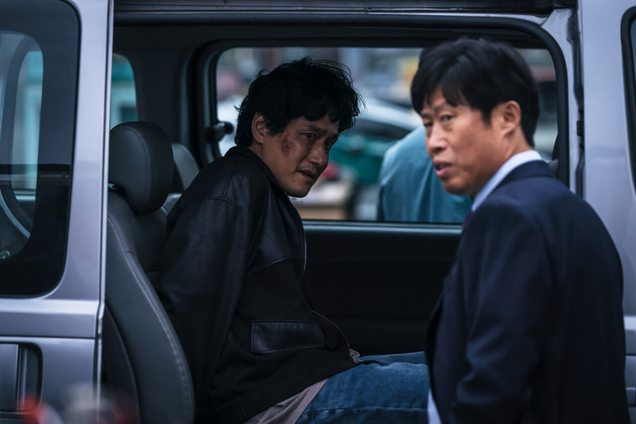 구관희에게 일부러 잡혀서 차에 수갑을 찬 채 올라타있는 오상재의 모습