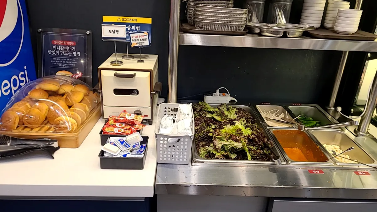 명륜진사갈비-실내-샐러드바에-야채와-음료기계-모닝빵이-세팅되어있다