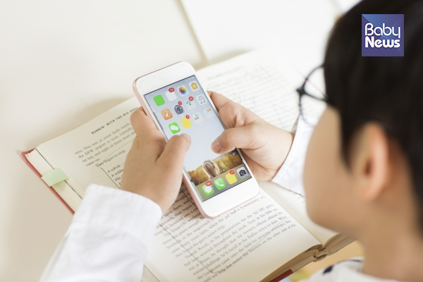 안경 쓴 아이가 스마트폰을 보는 사진