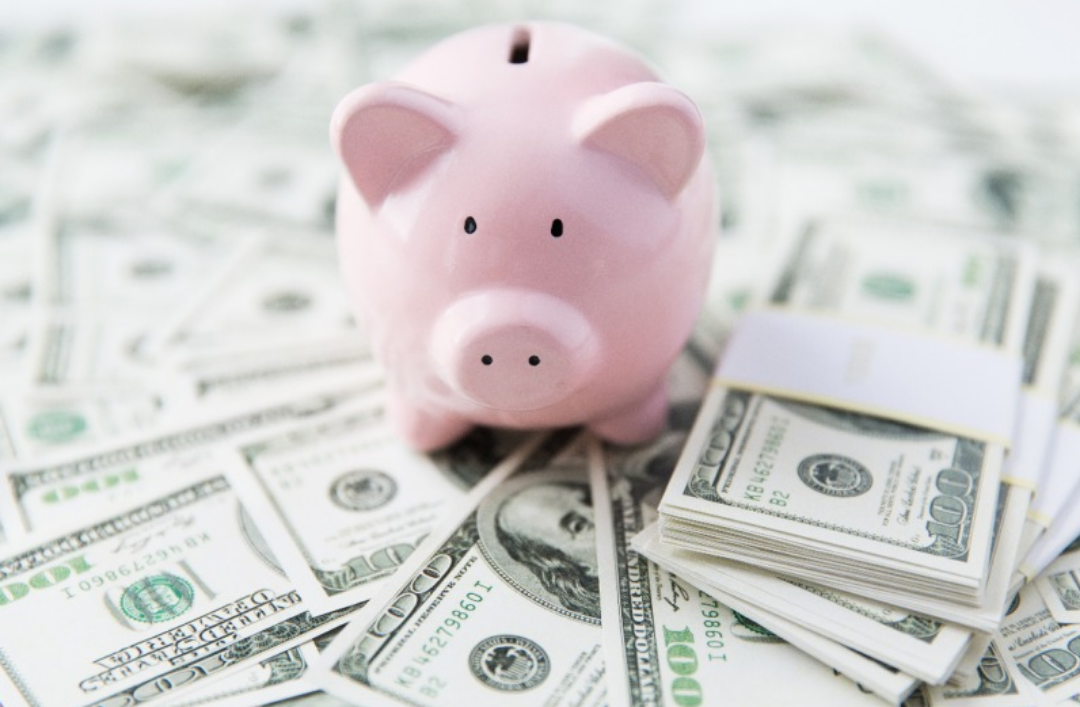 핑크색 돼지 저금통과 달러가 바닥에 널려있다.