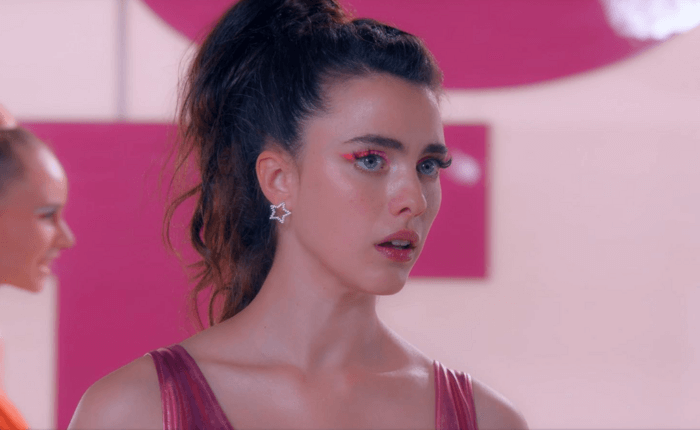 영화 서브스턴스의 한 장면. 마가렛 퀄리가 분홍색 아이 메이크업과 별 모양 귀걸이를 한 채 정면을 응시하고 있다.