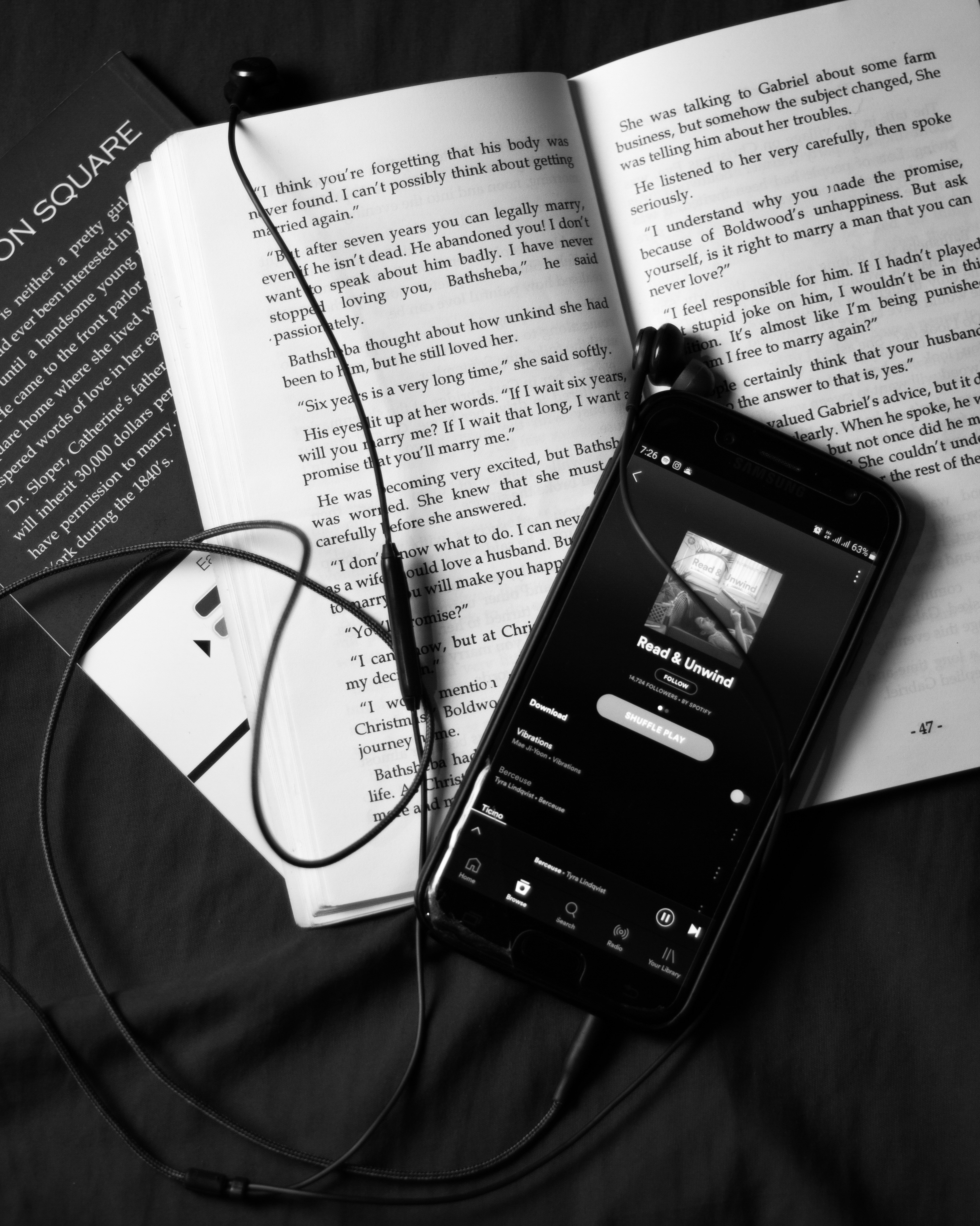 책 위에 올려진 스마트폰과 이어폰, 오디오북을 들으며 영어 원서를 읽는 모습