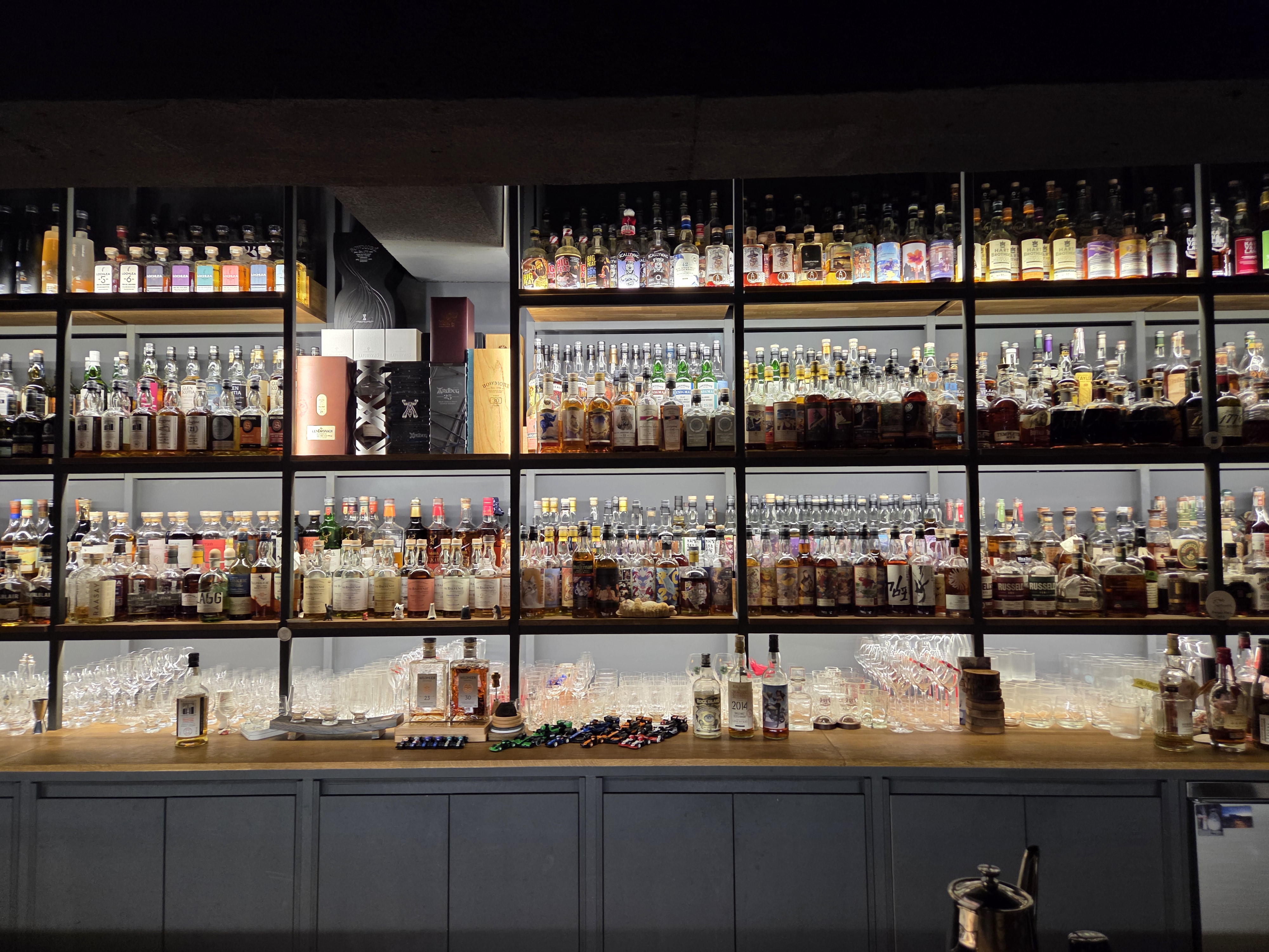 바밤(Bar Bam) 카운터석 전경&amp;#44; 조명 아래 진열된 다양한 위스키 병들이 보이는 바 공간