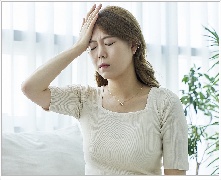 한쪽 이마에 손바닥을 올리고 두 눈을 감고 다소 힘든 표정을 짓고 있는 여성의 모습