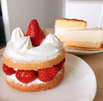 햄버거같이 디저트가 쌓여있는 동그란 케이크 쿠키 슈가, 딸기, 쿠키 그리고 제일 위에 크림과 딸기 한개가 놓여져 있다.