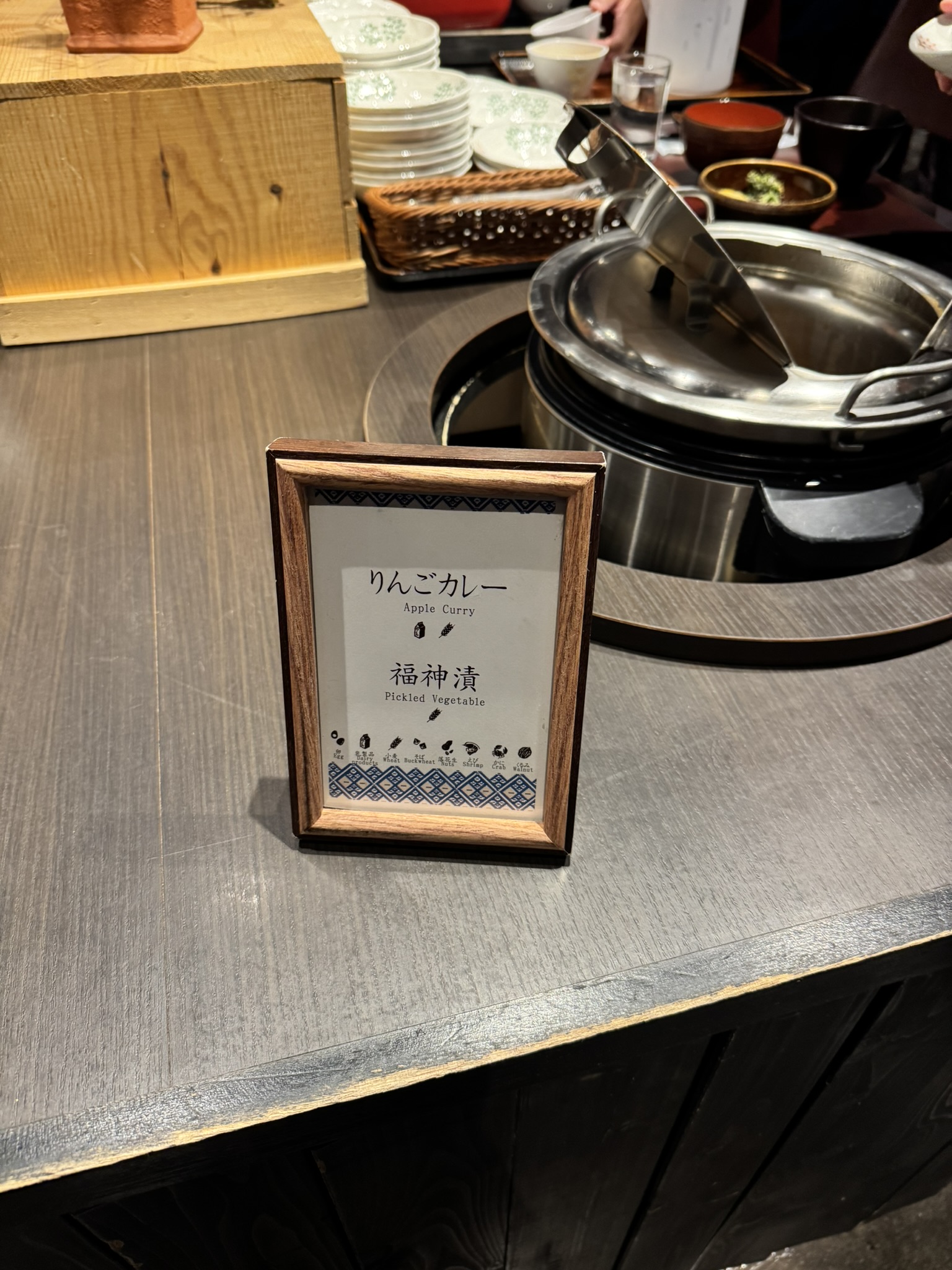 아오모리 특산물을 활용한 '사과 카레(Apple Curry)' 코너. 나무 프레임 액자에 메뉴 이름과 알레르기 유발 성분이 표시되어 있으며, 뒤편에 카레가 담긴 대형 보온 솥이 보임.