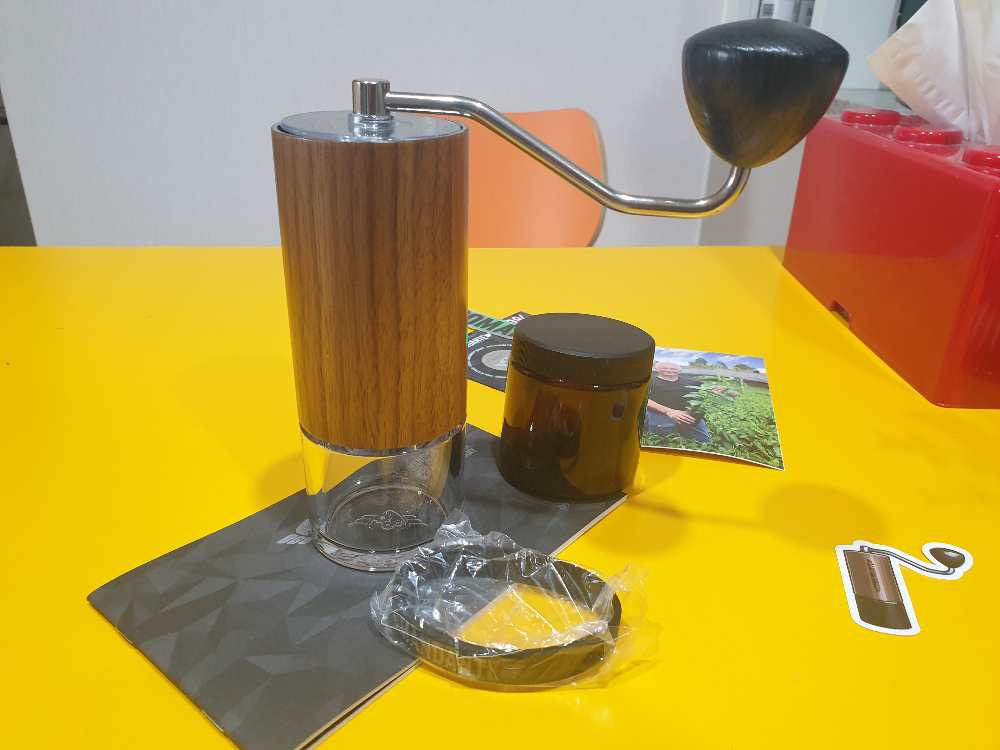 노란 테이블 위에 코만단테 그라인더 원두 보관통 그리고 설명서가 놓여있다.