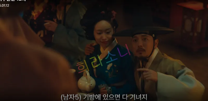 전통 복장을 한 남성이 기생복을 입은 여성을 어깨에 손을 두른 채 술병과 찻잔이 놓인 탁자 옆에 앉아 있다. 자막 