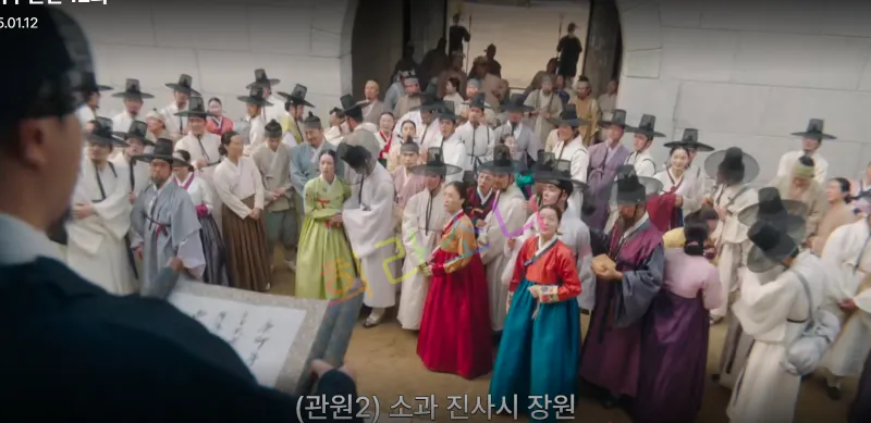 관리들이 검은 도포를 입고 문 앞에 모인 사람들 앞에서 성과 관련된 발표를 하고 있다. 다양한 색상의 한복을 입은 남녀가 모여 발표를 경청하고 있는 모습. 자막 