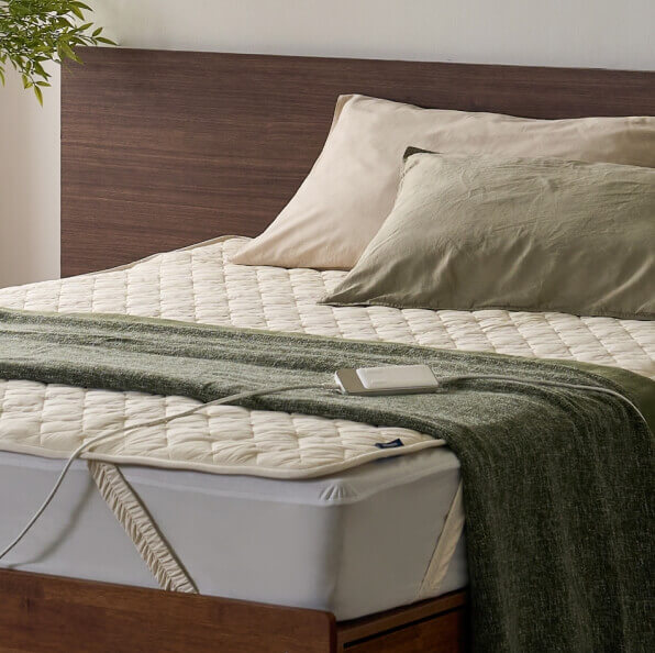 침대 위 초록색 이불과 흰색 전기매트