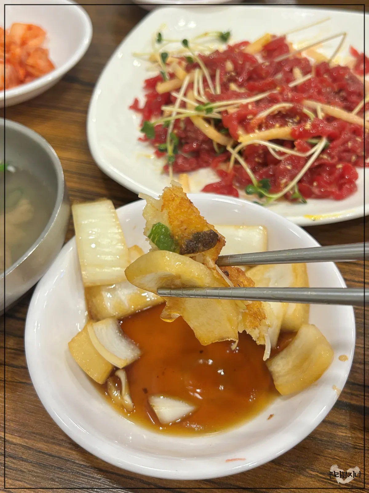 종로-통큰누이네-육회빈대떡-메인-메뉴-누이네-세트-중-녹두빈대떡을-양파에-싸서-젓가락으로-들고있는-모습