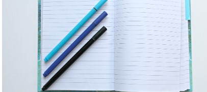 펼쳐져 있는 빈 공책과 그 위에 세자루의 펜이 놓여있는 사진