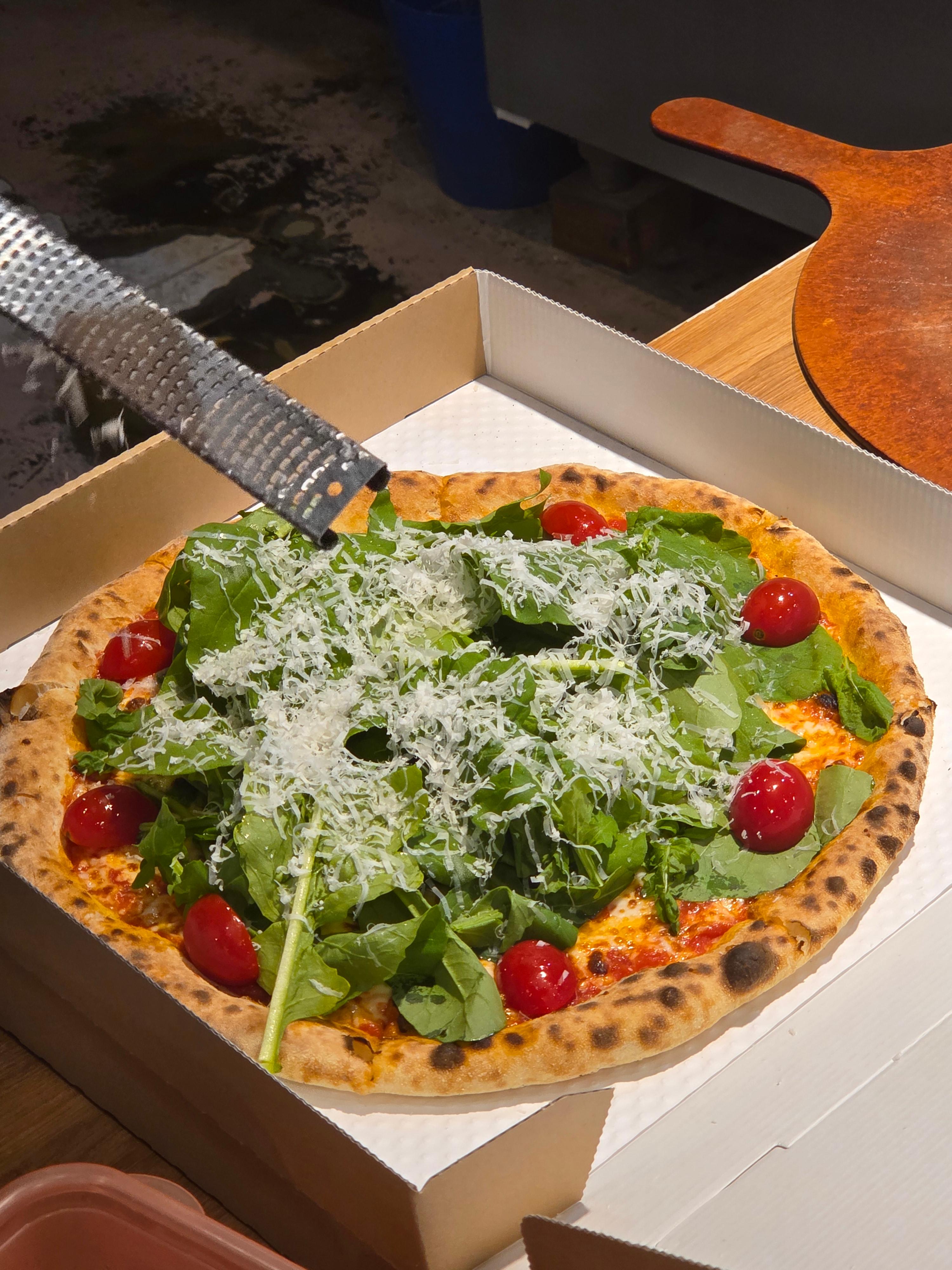 루꼴라 피자 위에 잘 갈아낸 그라나파다노 치즈를 솔솔 뿌려 마무리하는 장면