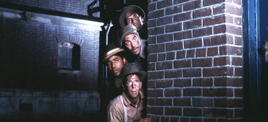 벽 뒤에 숨은 네 남자가 어딘가를 염탐하는 모습