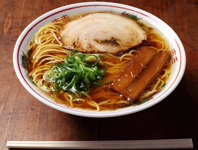 검은색의 국물을 띄고 있는 라면이 그릇안에 들어가 있고 위로 차슈와 초록색 대파가 올라가 있다
