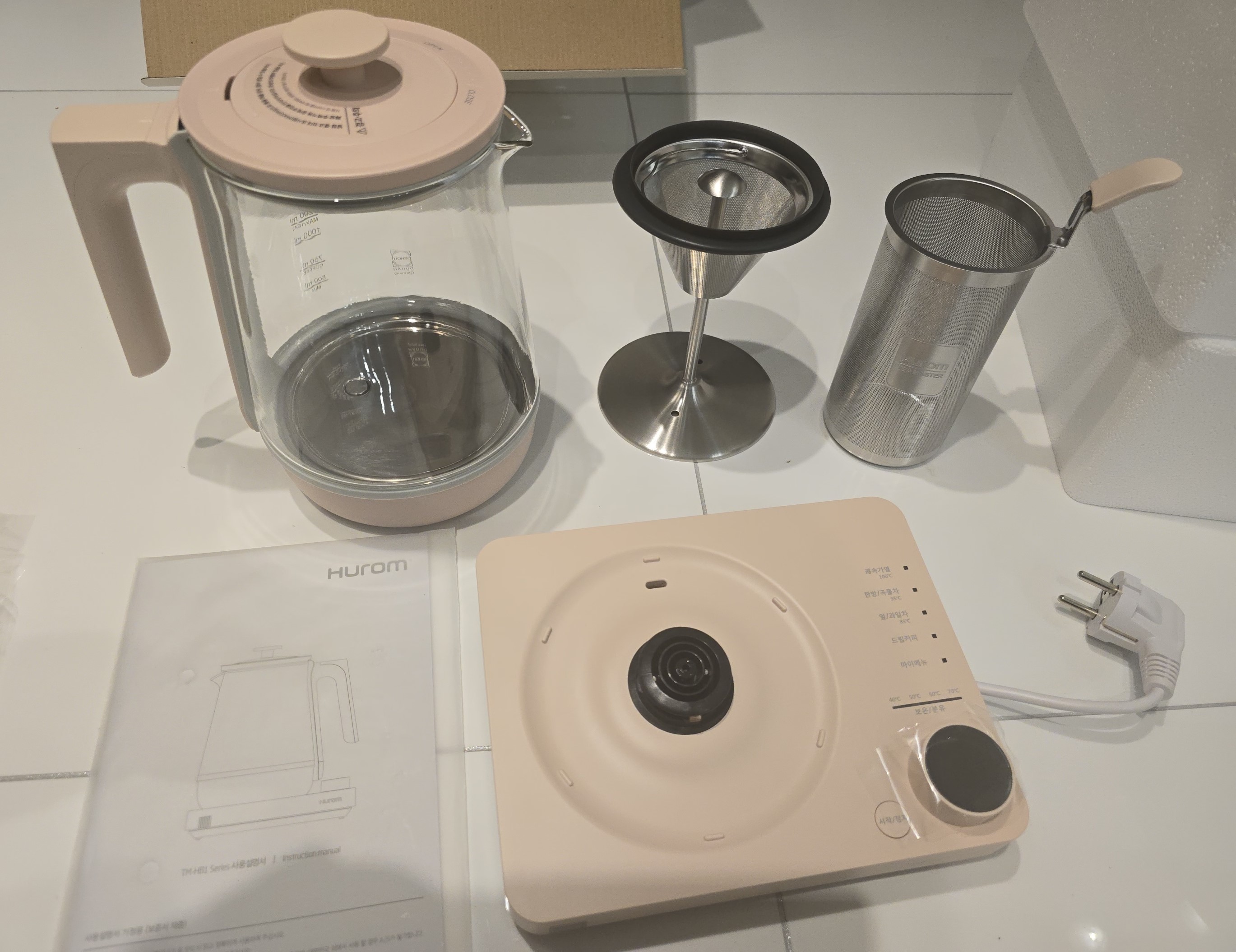 촌스럽지 않은 인디핑크 빛의 휴롬 멀티 티마스터의 구성품. 드립포트, 차 우림 바구니, 설명서의 구성품으로 이루어짐
